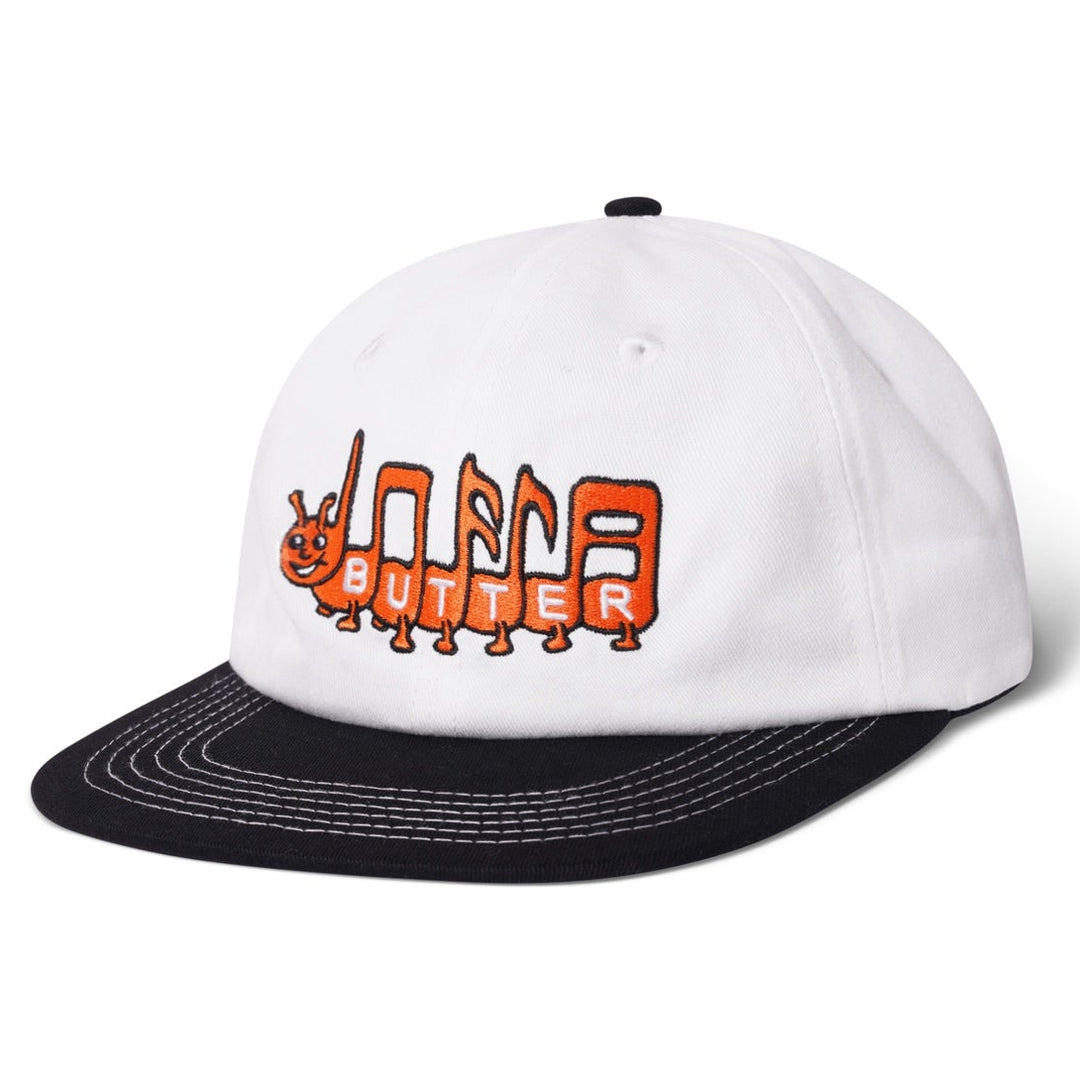 White 6 panel denim cap with orange and black 'Butter Goods' logo embroidery on the front and a black adjustable strap.