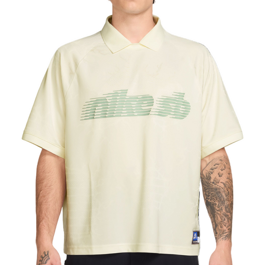 Man wearing a light-colored polo shirt with a green logo on a white background