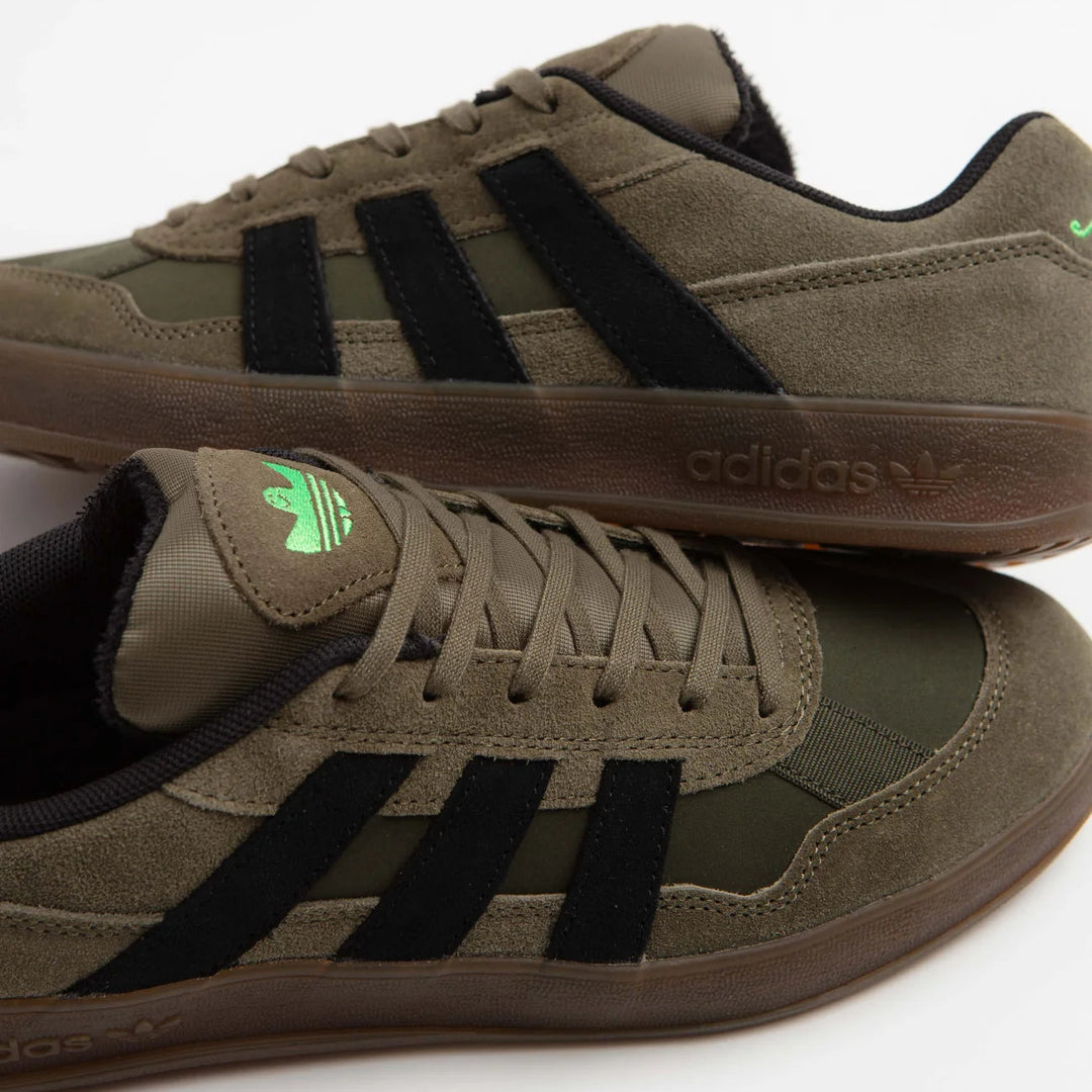 A pair of Adidas Zebra sneakers in olive green suede and mesh with black three-stripes, brown soles, and a small green trefoil logo on the tongue, shown on a white background.