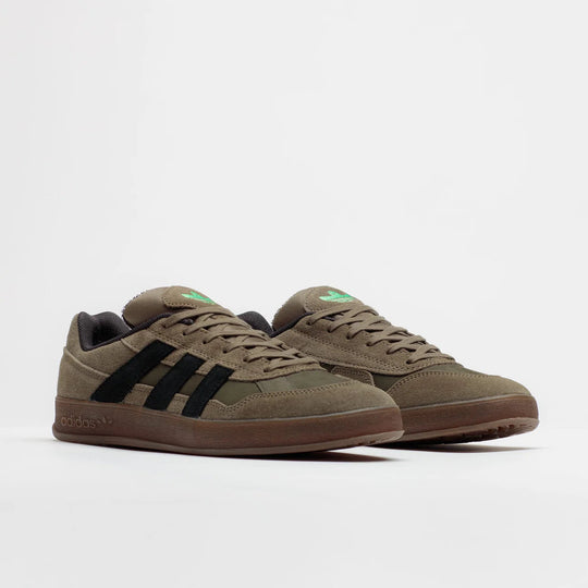 A pair of Adidas Samba sneakers in olive green suede with black three-stripes, brown midsoles, and small green tongue accents, photographed on a clean white studio background.