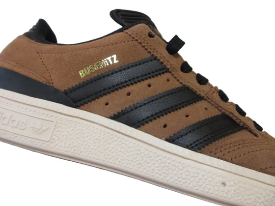 Brown sneaker with black stripes and visible brand logos on a gray background