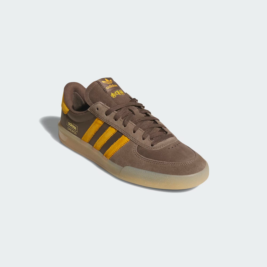 A single Adidas Zebra sneaker in brown suede with yellow stripes and a gum sole, photographed on a light gray background.