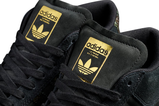 Black Adidas sneakers with gold logos on a white background