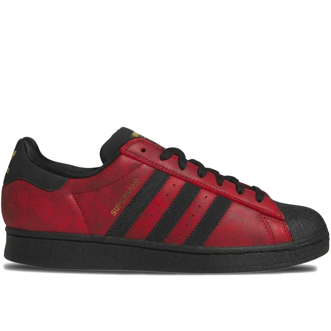 Adidas Superstar sneaker in red and black, featuring the classic three stripes, a red leather upper, black laces, and a black rubber toe cap and sole, shown in a side profile on a white background.