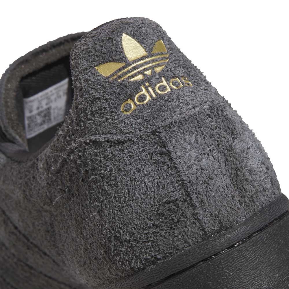 Close-up of a gray Adidas sneaker with gold logo on a white background