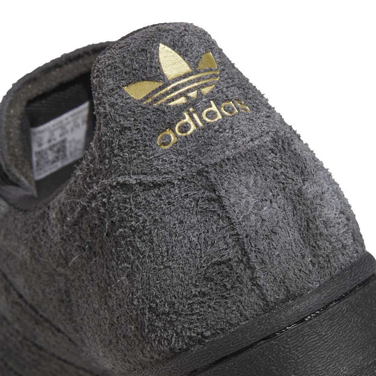 Close-up of a gray Adidas sneaker with gold logo on a white background