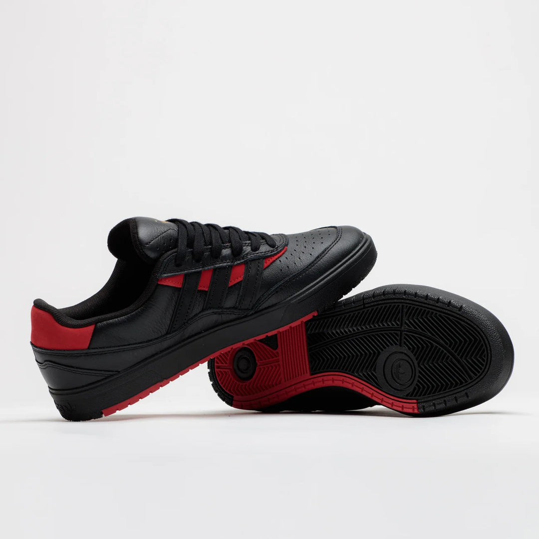 A pair of black low-top sneakers with vibrant red accents, including the side stripes, heel tab, and outsole, displayed on a clean white studio background.