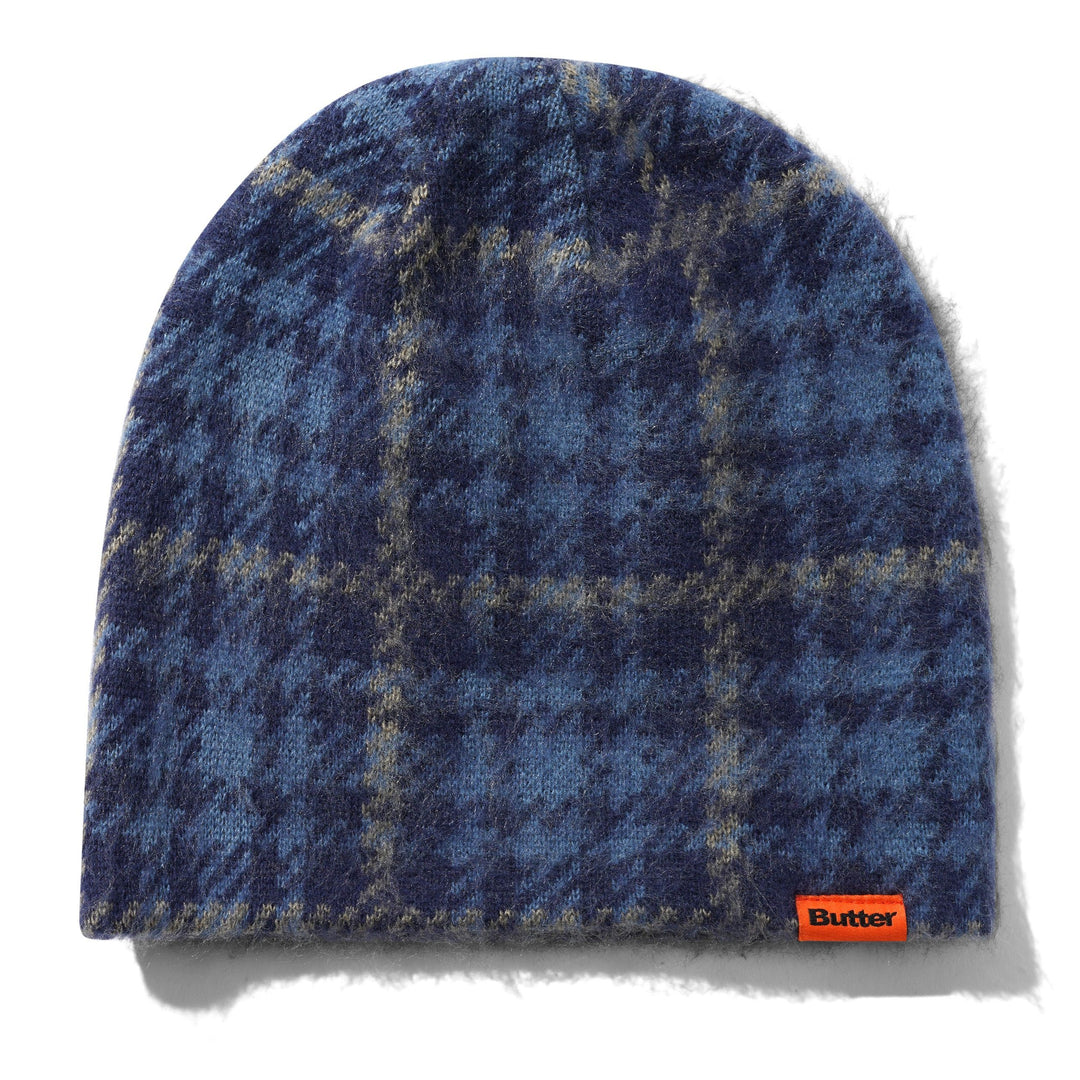 A blue and navy plaid knit beanie hat with a soft fuzzy texture, featuring a small orange Button brand tag on the lower right edge, set against a plain white background.