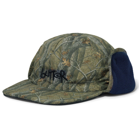 A camouflage 5-panel camp cap with a dark navy blue fleece ear flap and a black embroidered &