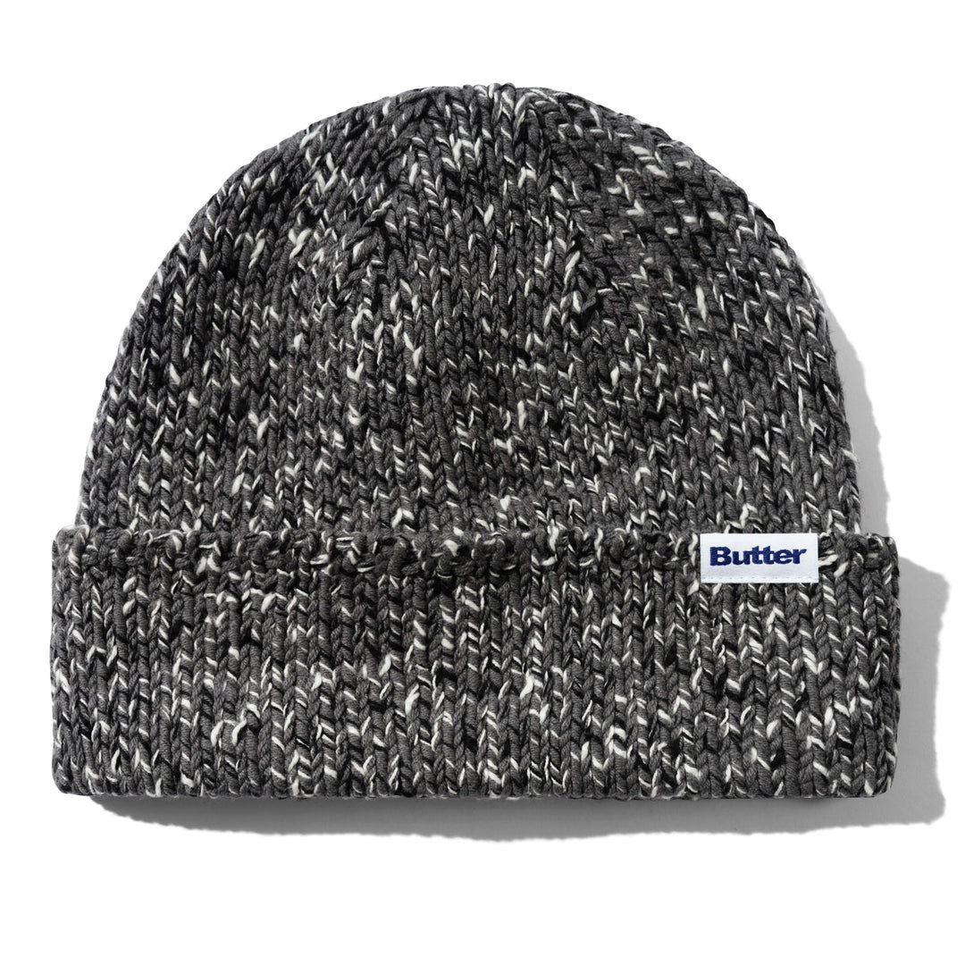 A marled black and white knit beanie hat with a folded cuff, featuring a small white 'Butter' brand label on the side, set against a plain white background.