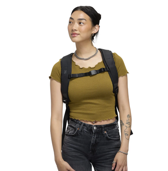 Woman wearing a mustard yellow top and black backpack on a white background