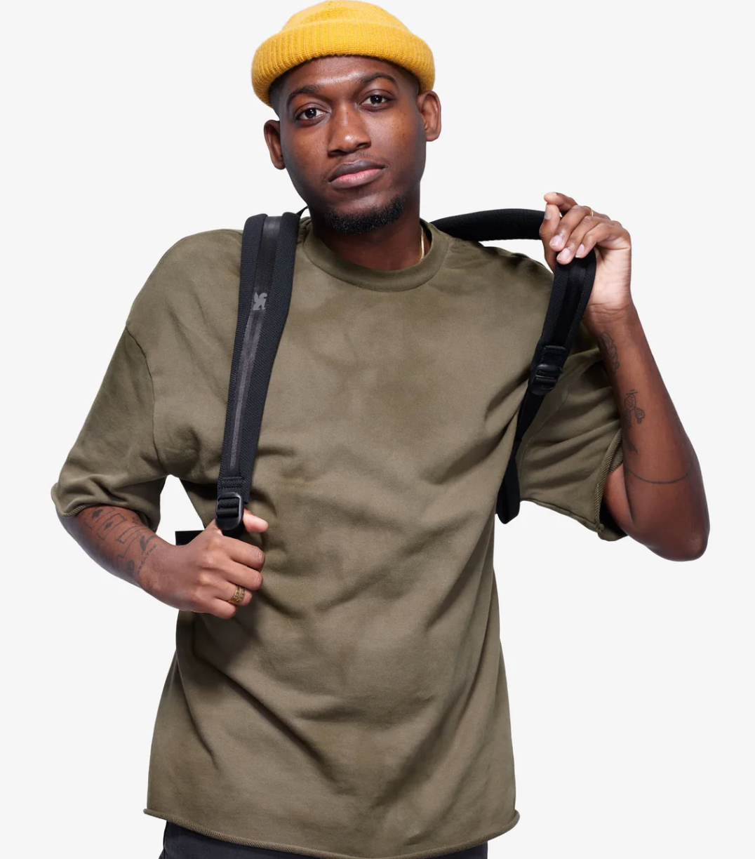 Man wearing a green t-shirt and yellow beanie holding a black bag against a white background