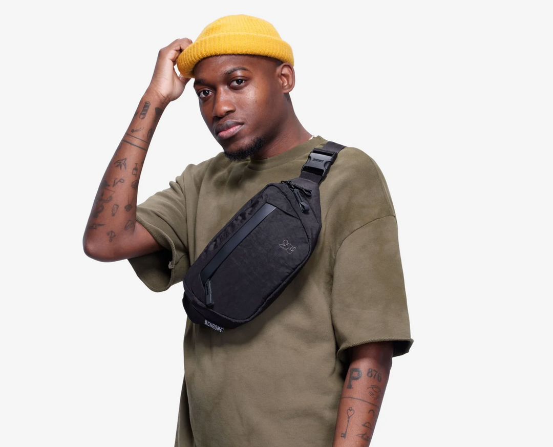 Man wearing a yellow beanie and green shirt with a black sling bag on a white background