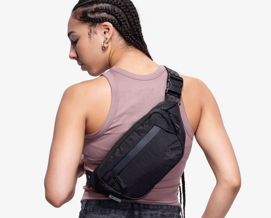 Person wearing a black sling bag on a plain background