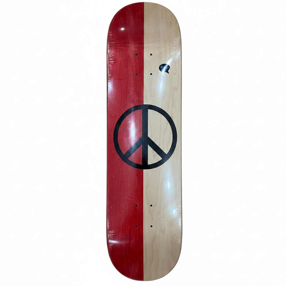 A skateboard deck with a split red and natural wood design, featuring a large black peace sign in the center, photographed on a light wood floor.
