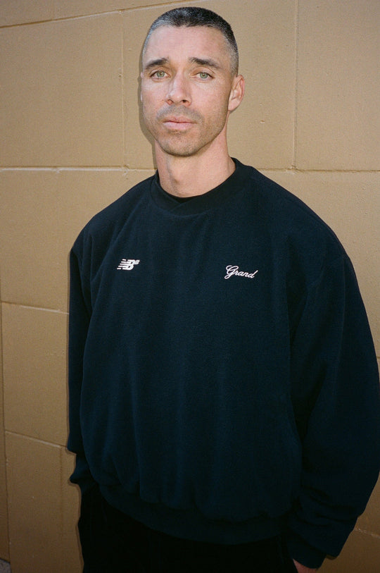 Man wearing a black sweatshirt with branding against a beige wall