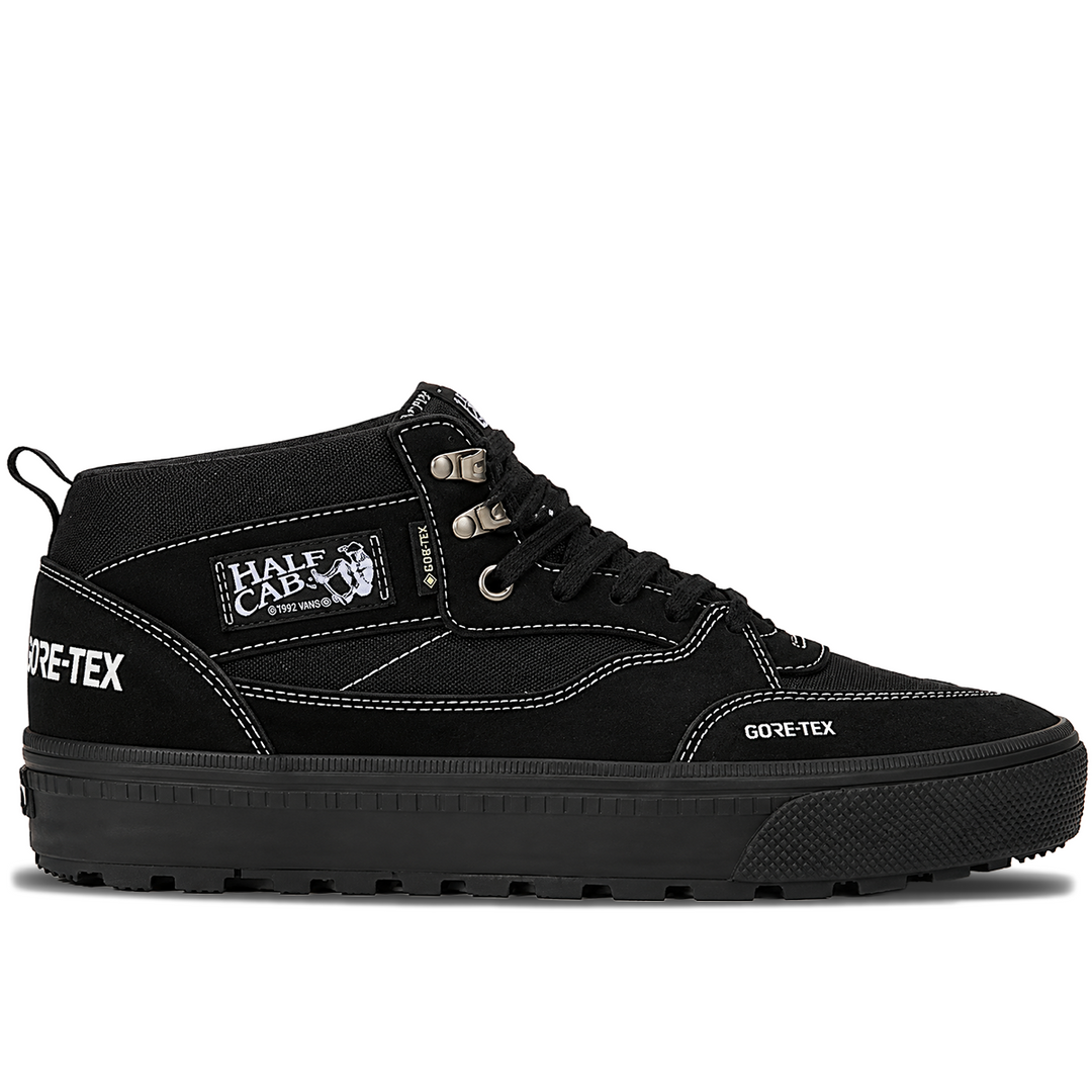 A black mid-top sneaker by Half Cab x Gore-Tex, featuring a canvas and suede upper, black laces, white contrast stitching, and a thick black sole with a rugged tread.