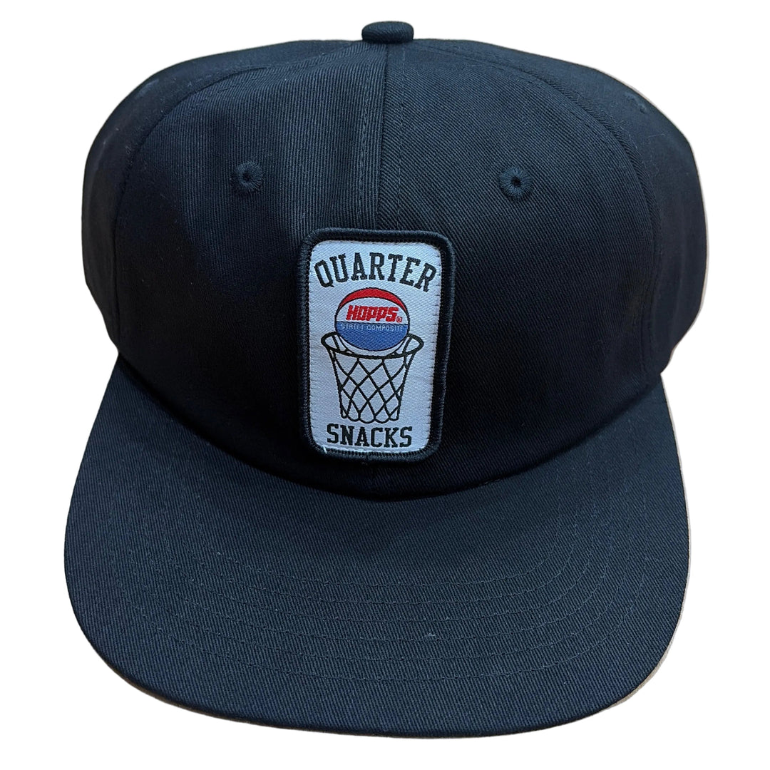 A black baseball cap with a rectangular embroidered patch on the front that reads 'QUARTER SMACKS' around a basketball graphic, placed on a light wood floor.