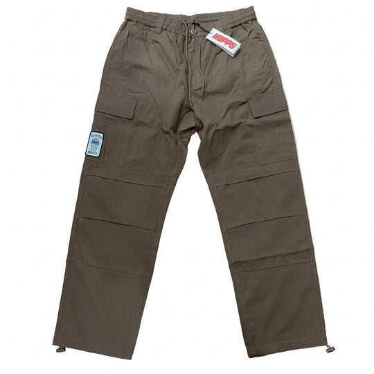 A pair of brown cargo pants laid flat on a light wood floor, featuring multiple utility pockets and a white brand tag near the waistband.
