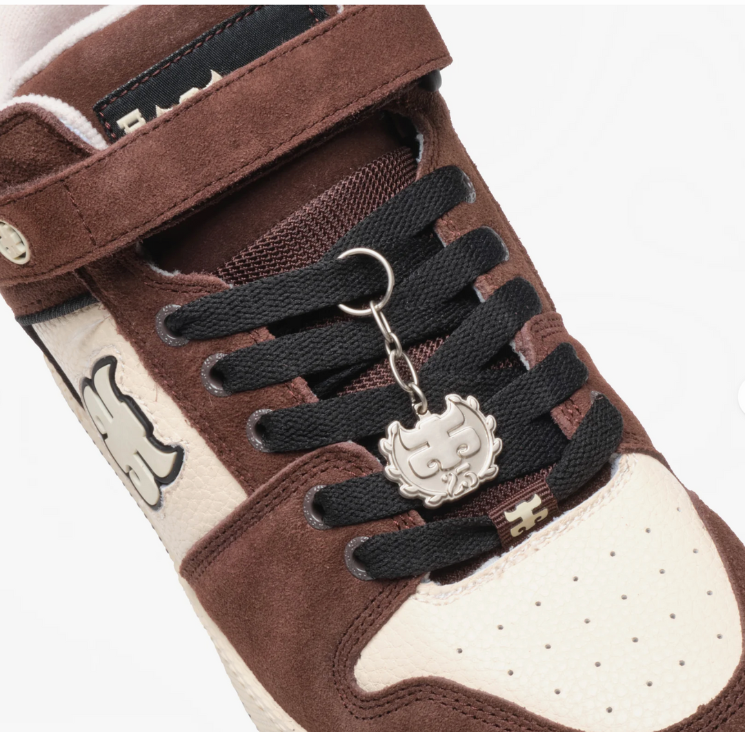 Brown and white sneaker with black laces and a silver cat-shaped keychain on a white background