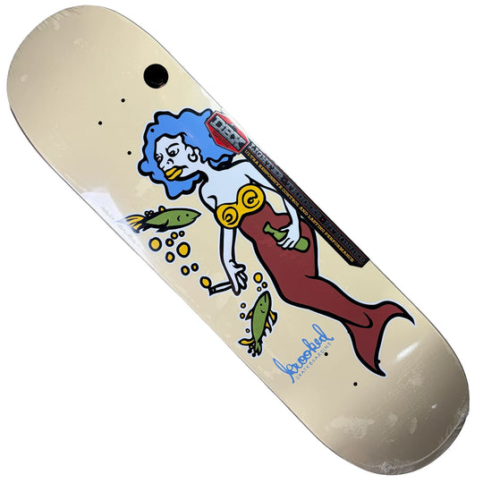A skateboard deck with a cream-colored base, featuring a graphic illustration of a mermaid with blue hair, a red tail, and yellow goggles, alongside fish and bubbles. The brand name &