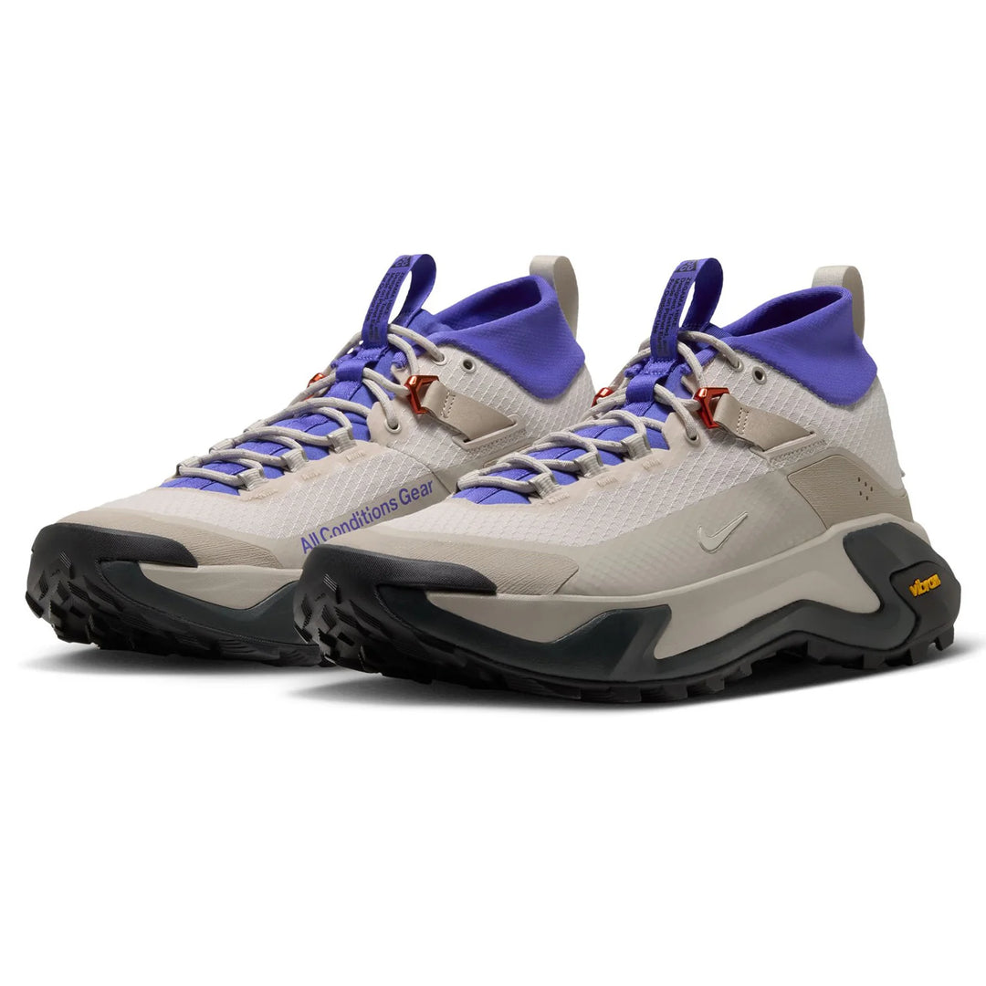 A pair of Nike hiking shoes in light beige and purple, featuring a textured mesh upper, purple laces, and a chunky black and beige Vibram sole.