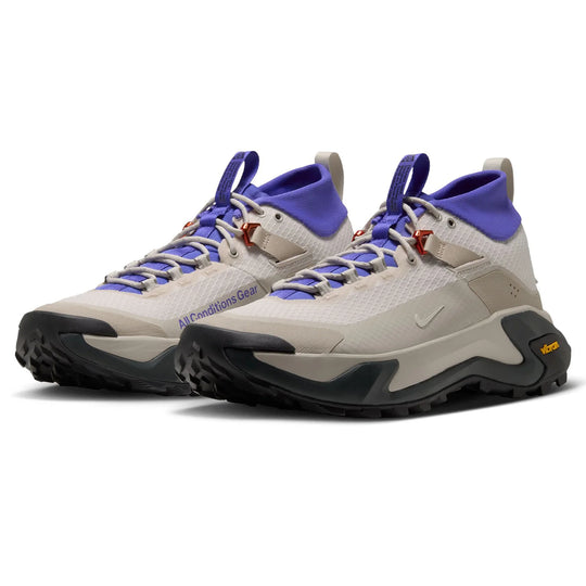 A pair of Nike hiking shoes in light beige and purple, featuring a textured mesh upper, purple laces, and a chunky black and beige Vibram sole.