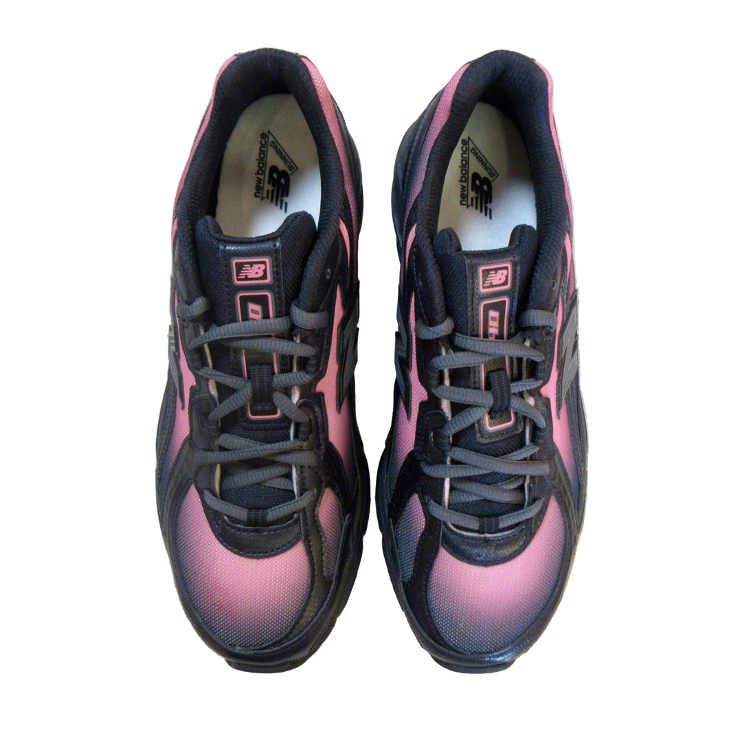 A pair of New Balance 574 athletic shoes in black and pink, photographed from a top-down perspective on a light gray concrete floor.