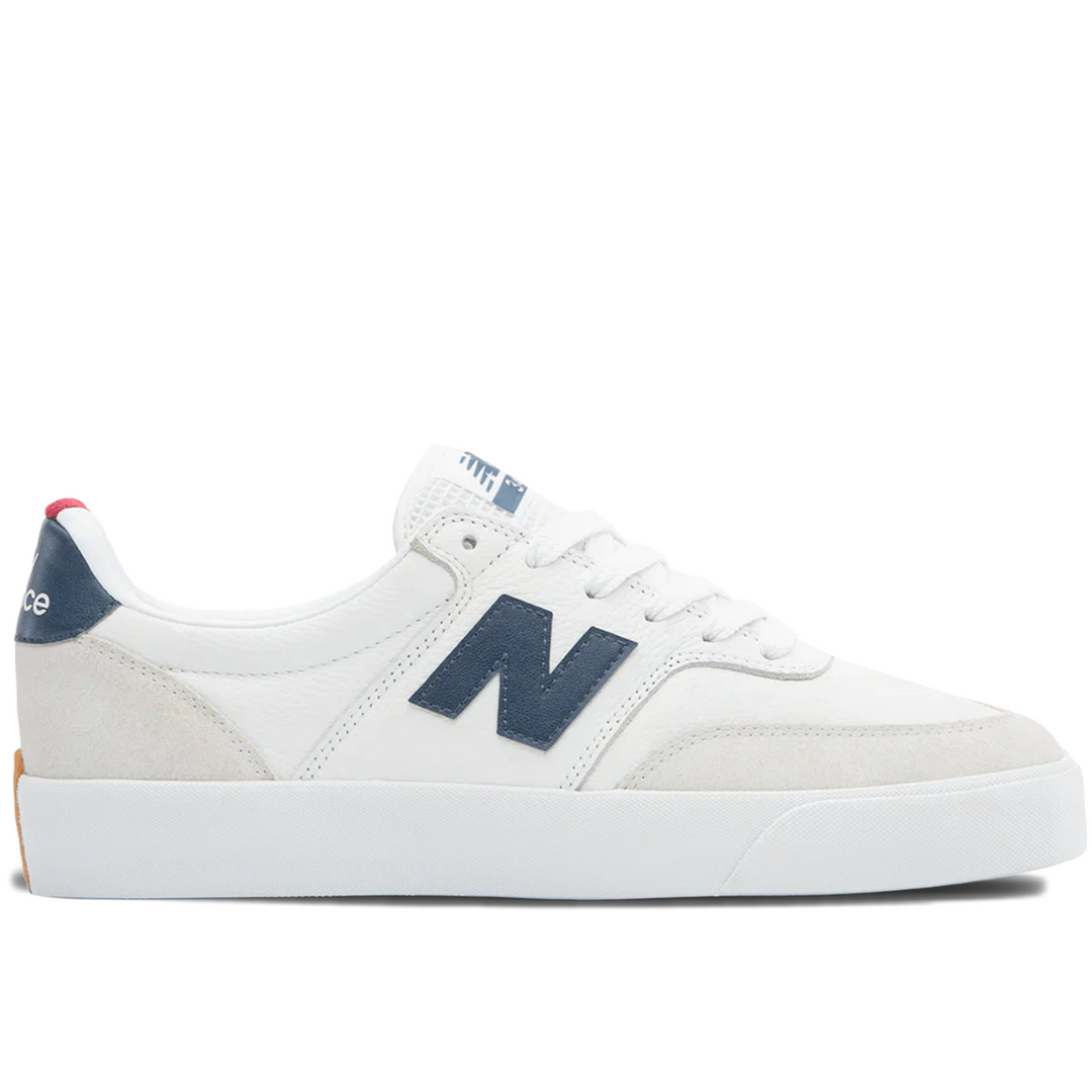 A white New Balance sneaker with navy blue accents, featuring the signature &