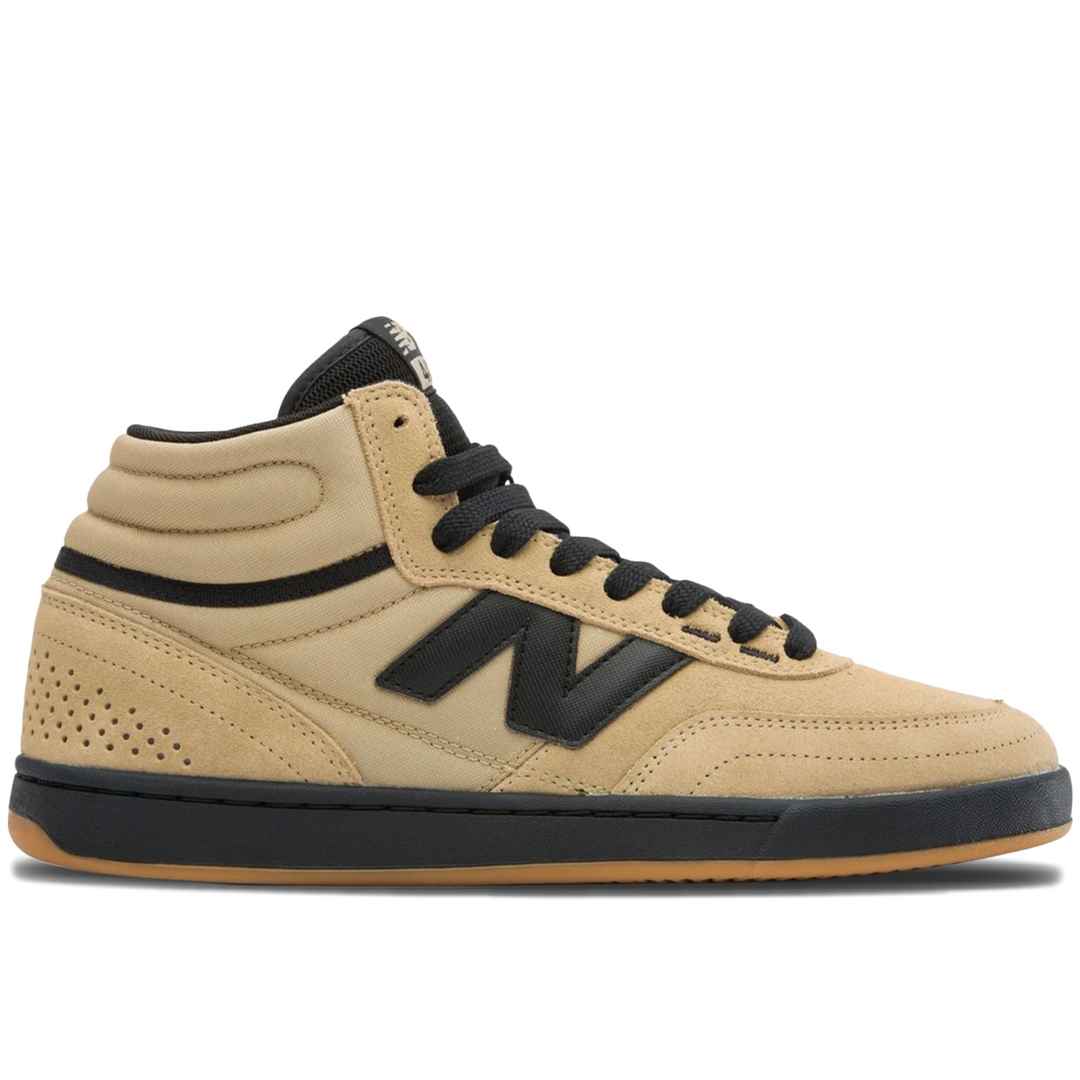 A New Balance mid-top sneaker in beige suede with black laces, a black side 'N' logo, and a black midsole, shown from a side profile on a white background.