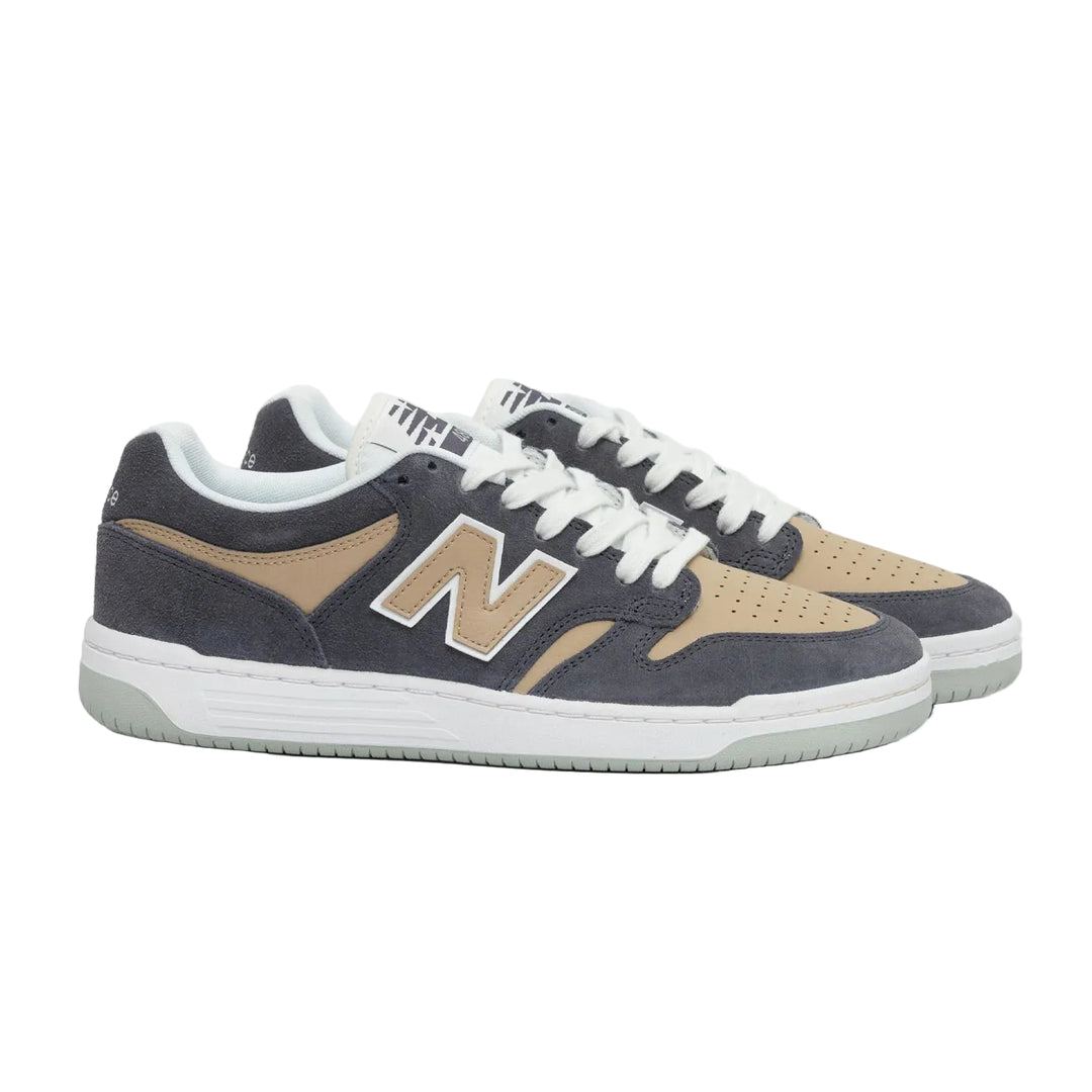 A pair of New Balance low-top sneakers in dark slate blue suede and tan suede, featuring white laces and a white midsole with a light green outsole, set against a plain light gray background.