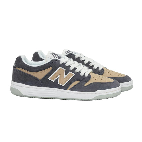 A pair of New Balance low-top sneakers in dark slate blue suede and tan suede, featuring white laces and a white midsole with a light green outsole, set against a plain light gray background.