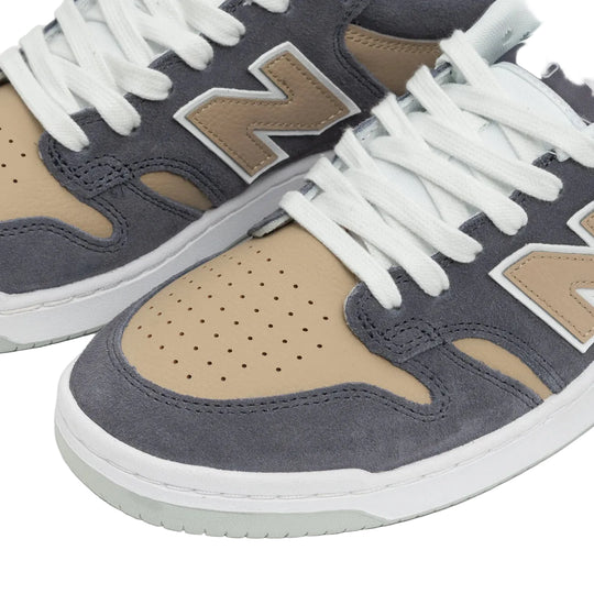 Close-up of a pair of New Balance 480 sneakers in dark gray suede and tan suede, featuring white laces and a white midsole.