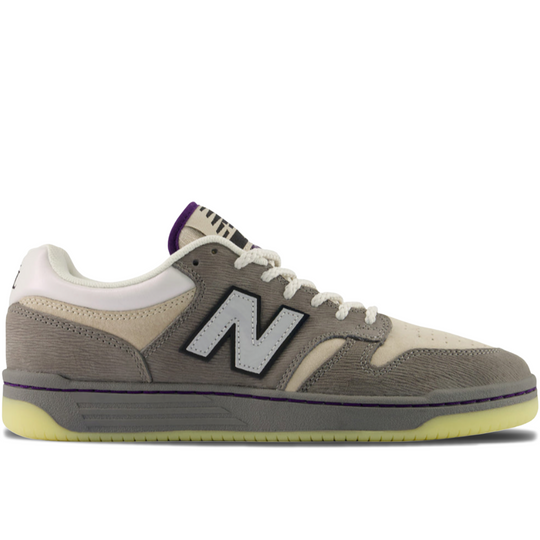 A New Balance sneaker in gray suede and canvas with cream panels, white laces, a purple collar accent, and a translucent yellow sole, shown in a side profile on a white background.