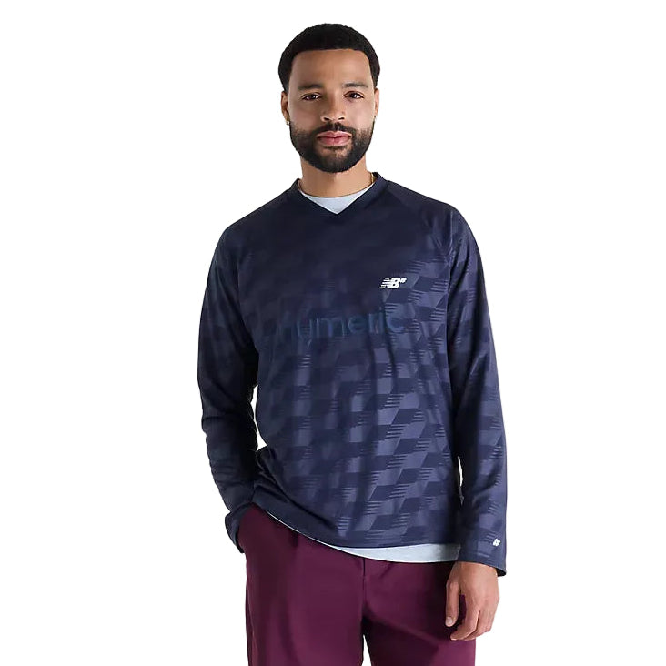A man modeling a dark navy long-sleeve athletic shirt with a subtle geometric pattern and a white New Balance logo on the chest, paired with maroon pants, against a plain white studio background.
