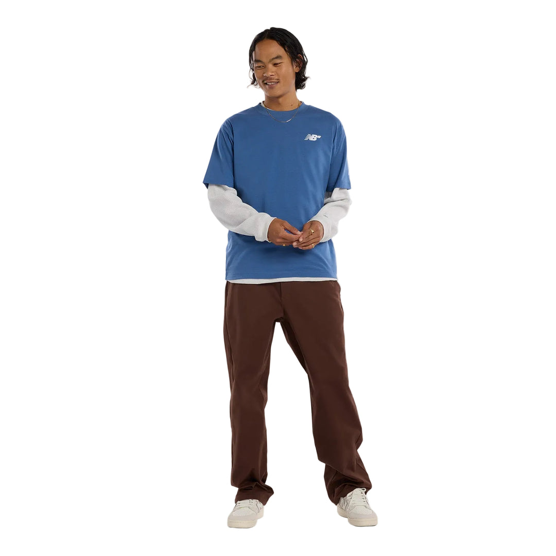 Skater wearing a blue long-sleeve shirt with a white nb# logo and brown pants 