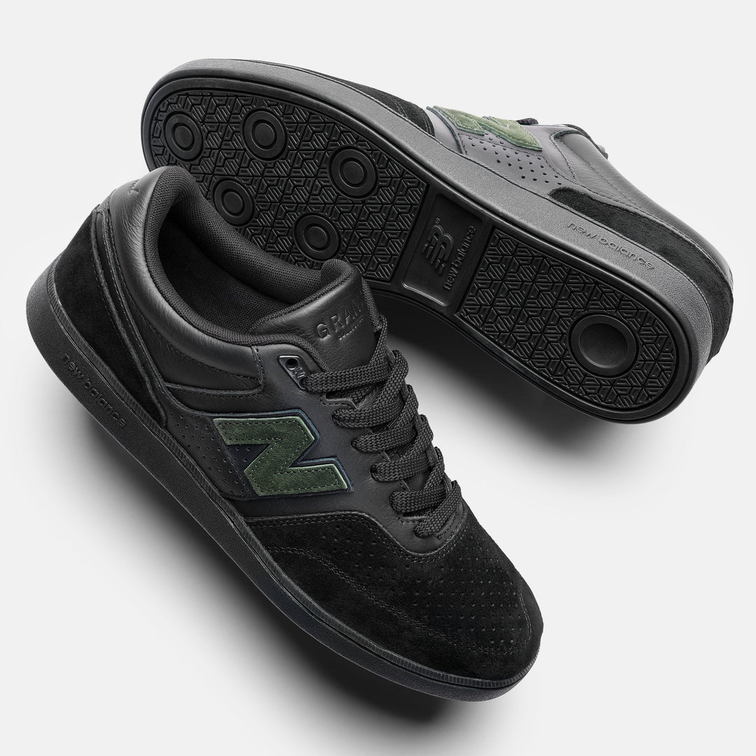 A pair of New Balance low-top sneakers in black, featuring a textured black upper, black laces, and a green &