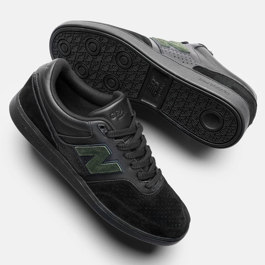 A pair of New Balance low-top sneakers in black, featuring a textured black upper, black laces, and a green &