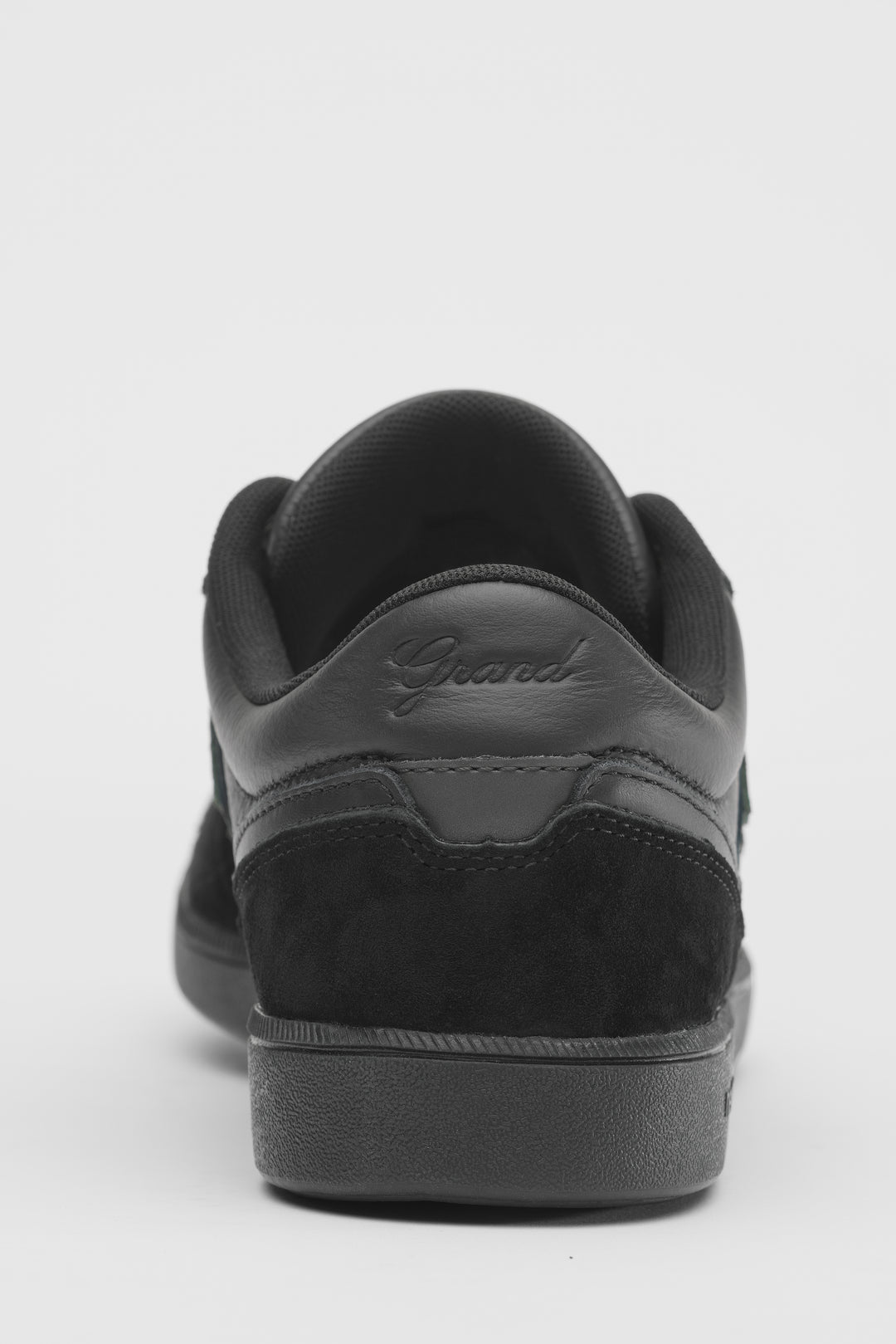 A black leather and suede sneaker shown from the rear three-quarter view, featuring a black sole and the brand name &