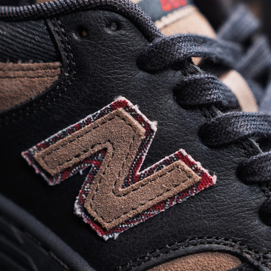Close-up of a black and brown sneaker with a logo on the side.