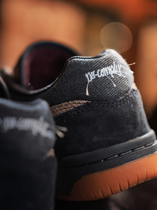 Close-up of a black sneaker with brown sole and white branding on a blurred background