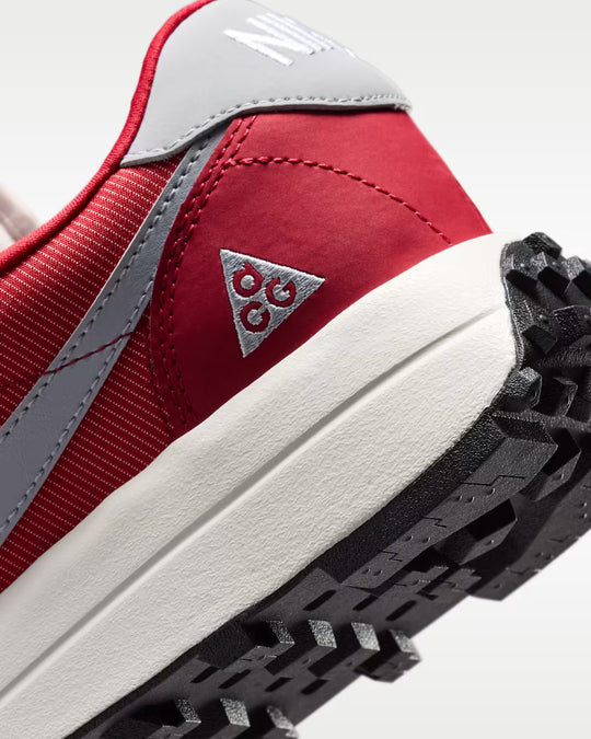 Close-up of a red and gray sneaker showing the heel, side stitching, triangular logo patch, white midsole, and black treaded outsole.