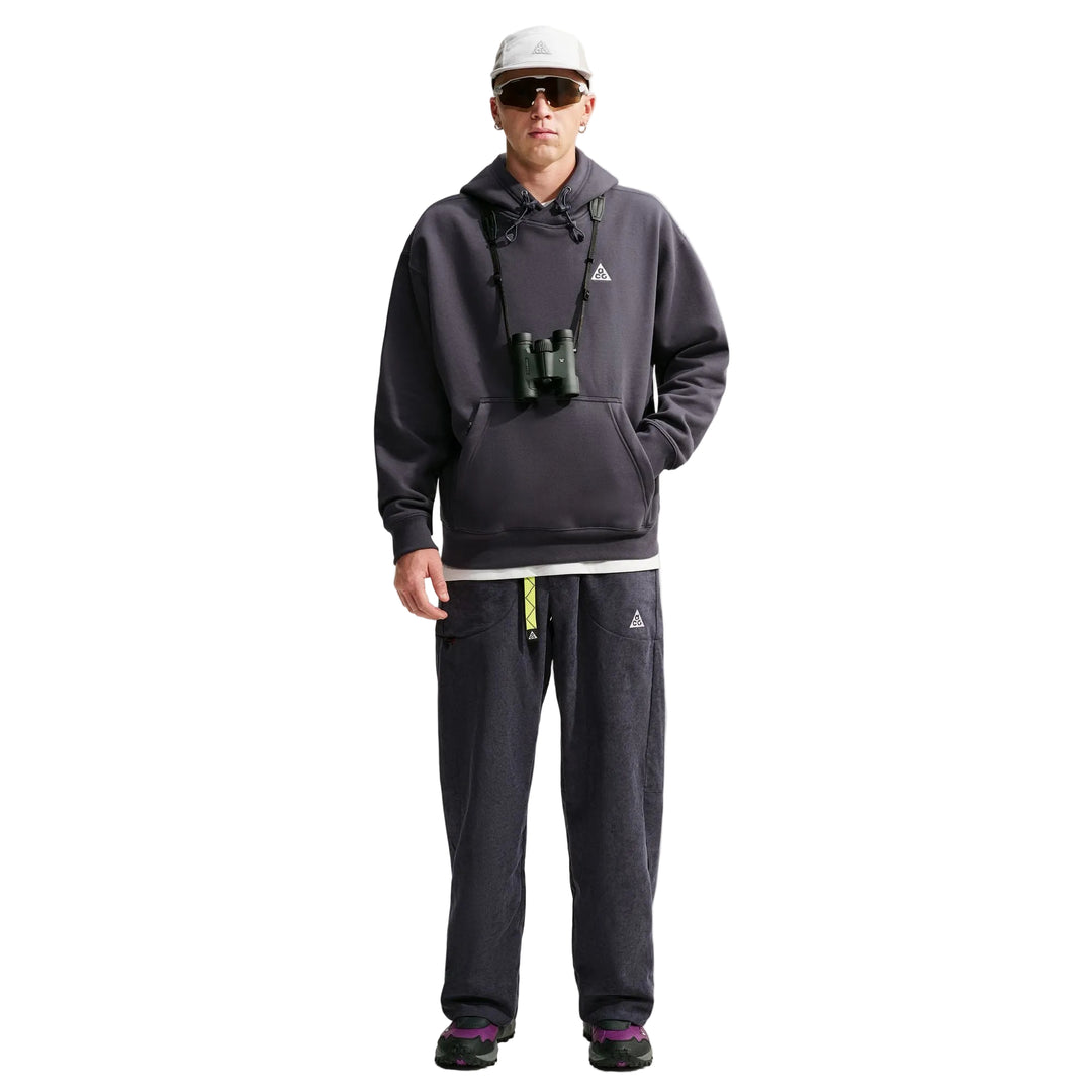 A man modeling a dark gray zip-up hoodie and matching dark gray sweatpants with a small white Adidas logo on the chest and thigh, styled with sunglasses, a white cap, and binoculars against a light gray studio background.