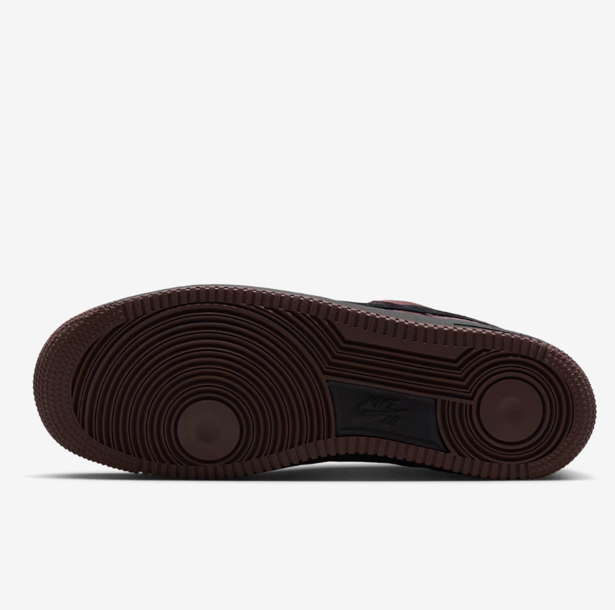 The outsole of a Nike Air Force 1 sneaker, showing a dark brown rubber tread with circular grooves and a black Nike Swoosh logo in the center, set against a light gray background.