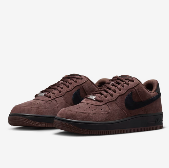 A pair of Nike Air Force 1 Low sneakers in a dark brown suede and black leather finish, displayed on a clean light gray background.