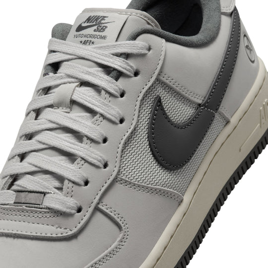 A close-up of a Nike Air Force 1 Low sneaker in light gray and dark gray, featuring a white midsole and a black outsole.
