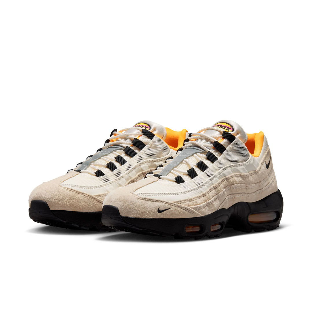 Pair of beige sneakers with black and orange accents on a white background