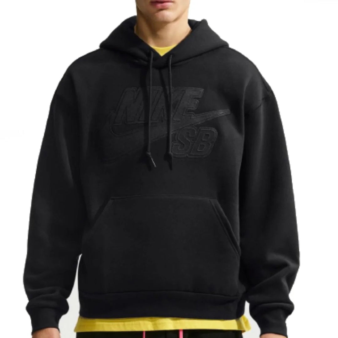 A man wearing a black Nike SB hoodie with a tonal black logo on the chest, layered over a yellow t-shirt and black sweatpants with pink drawstrings, against a plain white background.
