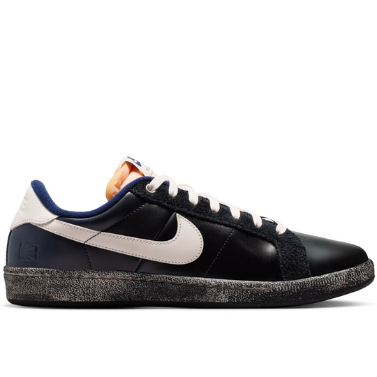 A Nike low-top sneaker in black leather with a cream-colored Swoosh, navy blue heel and collar details, white laces, and a distressed black sole.