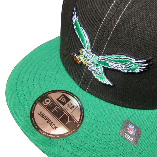 A green and black New Era 9FIFTY snapback cap featuring a green and white embroidered Philadelphia Eagles eagle logo on the front. The cap is photographed close-up on a dark textured surface, showing the green visor with a metallic bronze 9FIFTY sticker and an NFL tag.